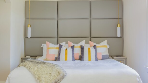 A bedroom with a large bed, a headboard with a padded design, two bedside tables, and a window.