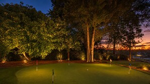 A golf course at dusk with illuminated trees and a sunset in the background.