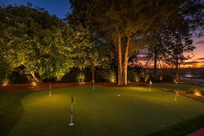 A golf course at dusk with illuminated trees and a sunset in the background.
