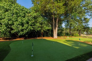 A golf course with a putting green, trees, and a clear sky.
