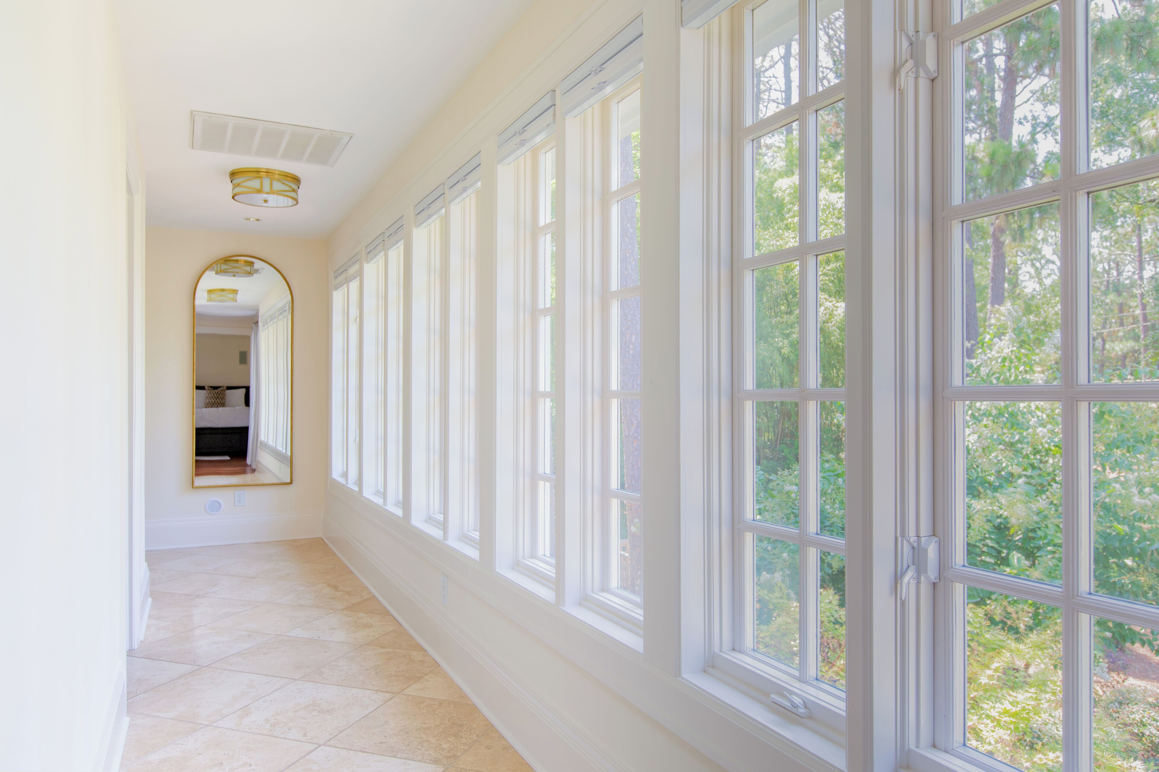 A hallway with large windows and a door leading to a room.