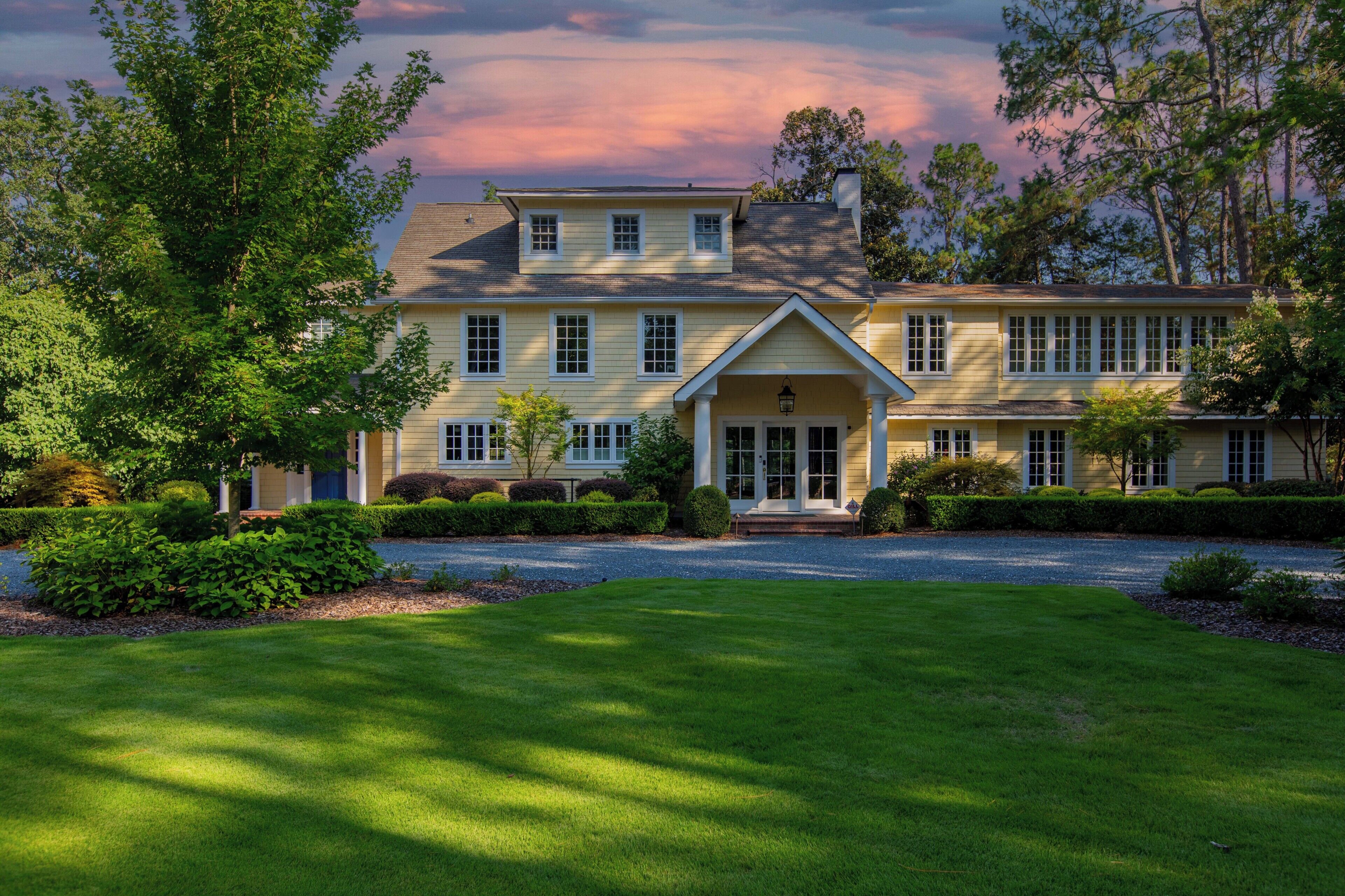 A two-story house with a front porch, surrounded by well-maintained lawns and trees.