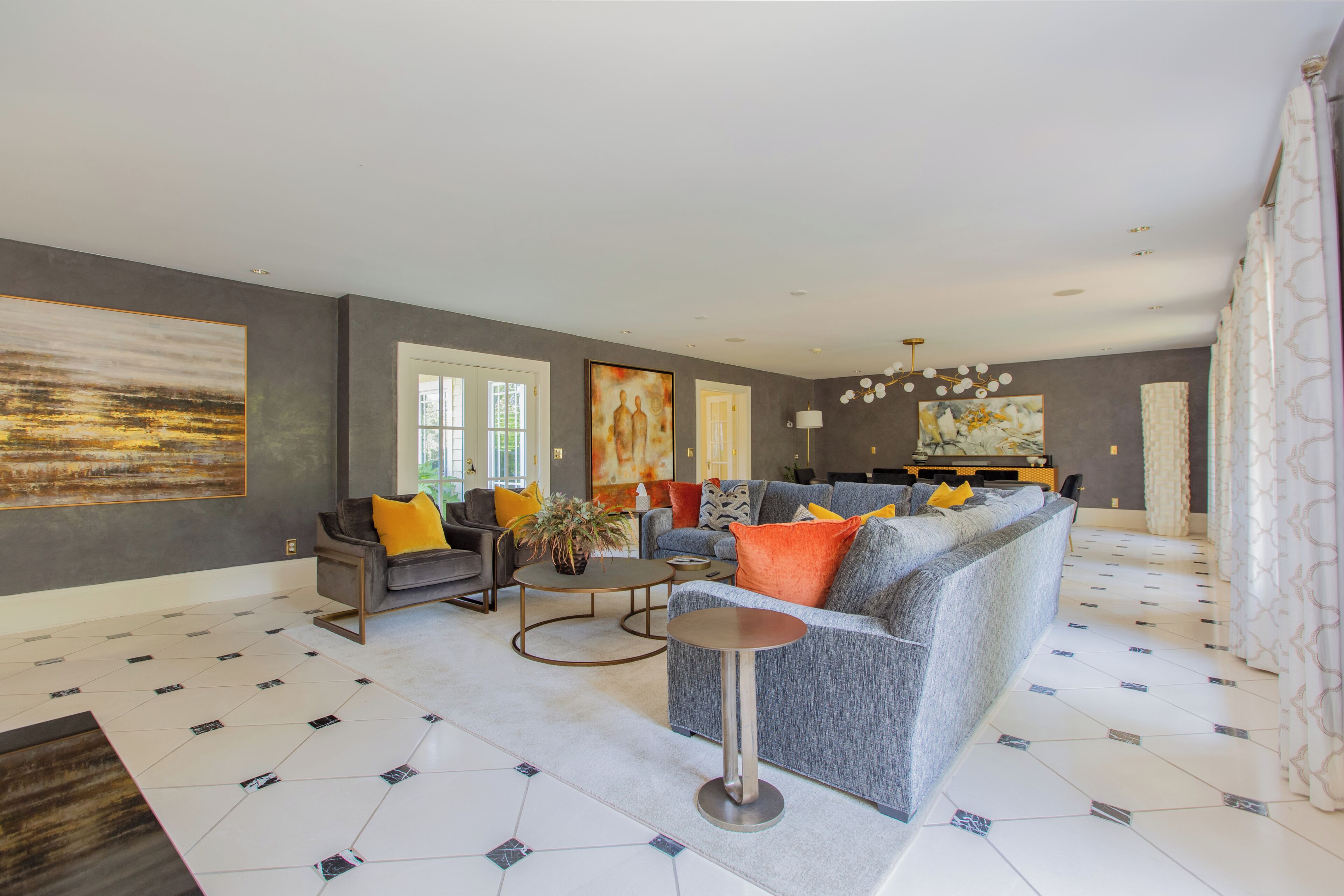 A modern living room with a grey sofa, a coffee table, and a dining area with a chandelier.