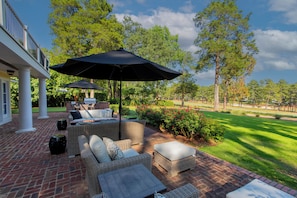 A patio with wicker furniture, a grill, and a view of a golf course.