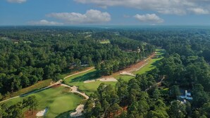 A golf course with multiple fairways and sand bunkers, surrounded by dense forest.