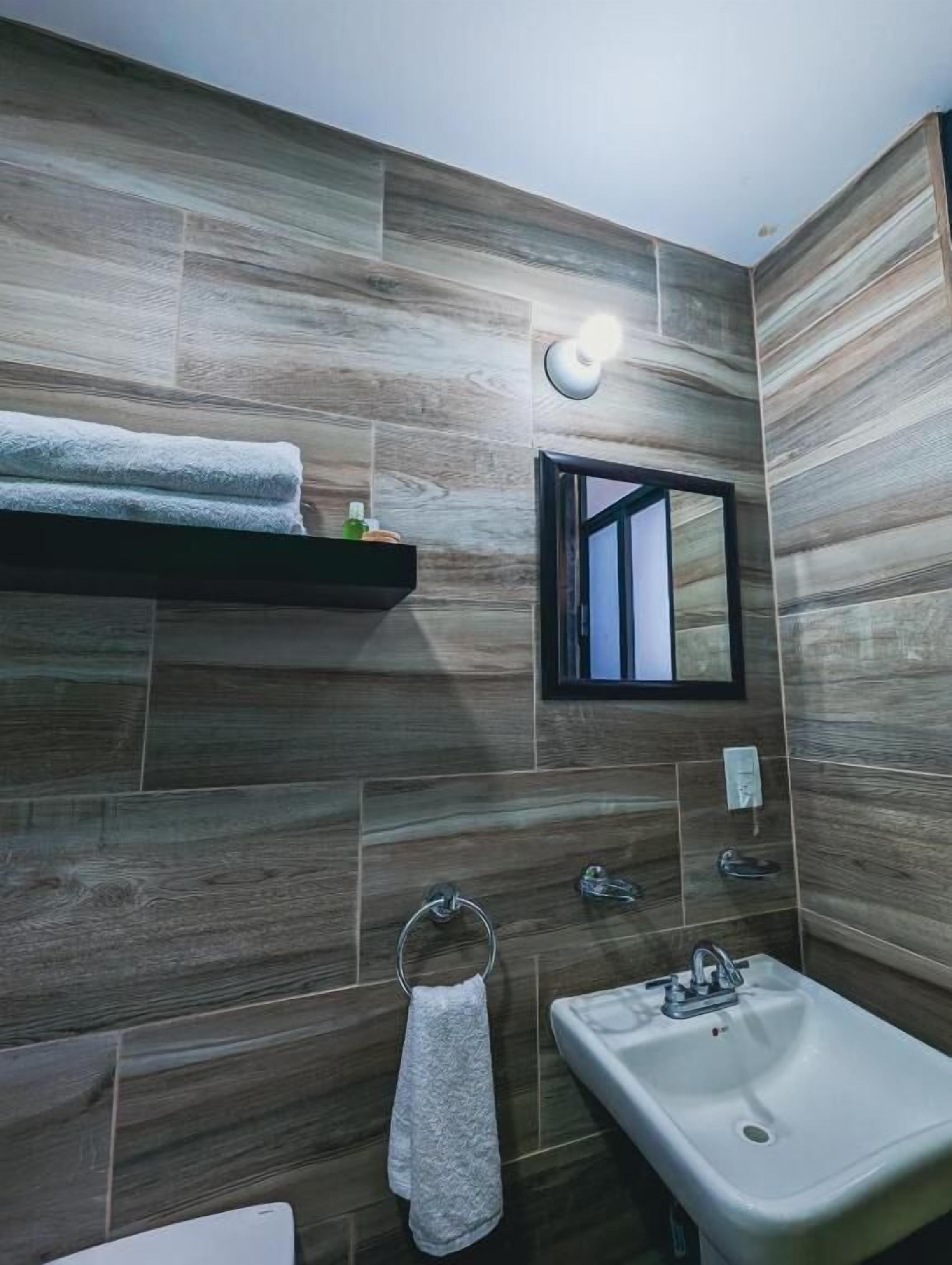 Een badkamer met een houten wand, een wastafel, een handdoekhouder en een plank met een handdoek.