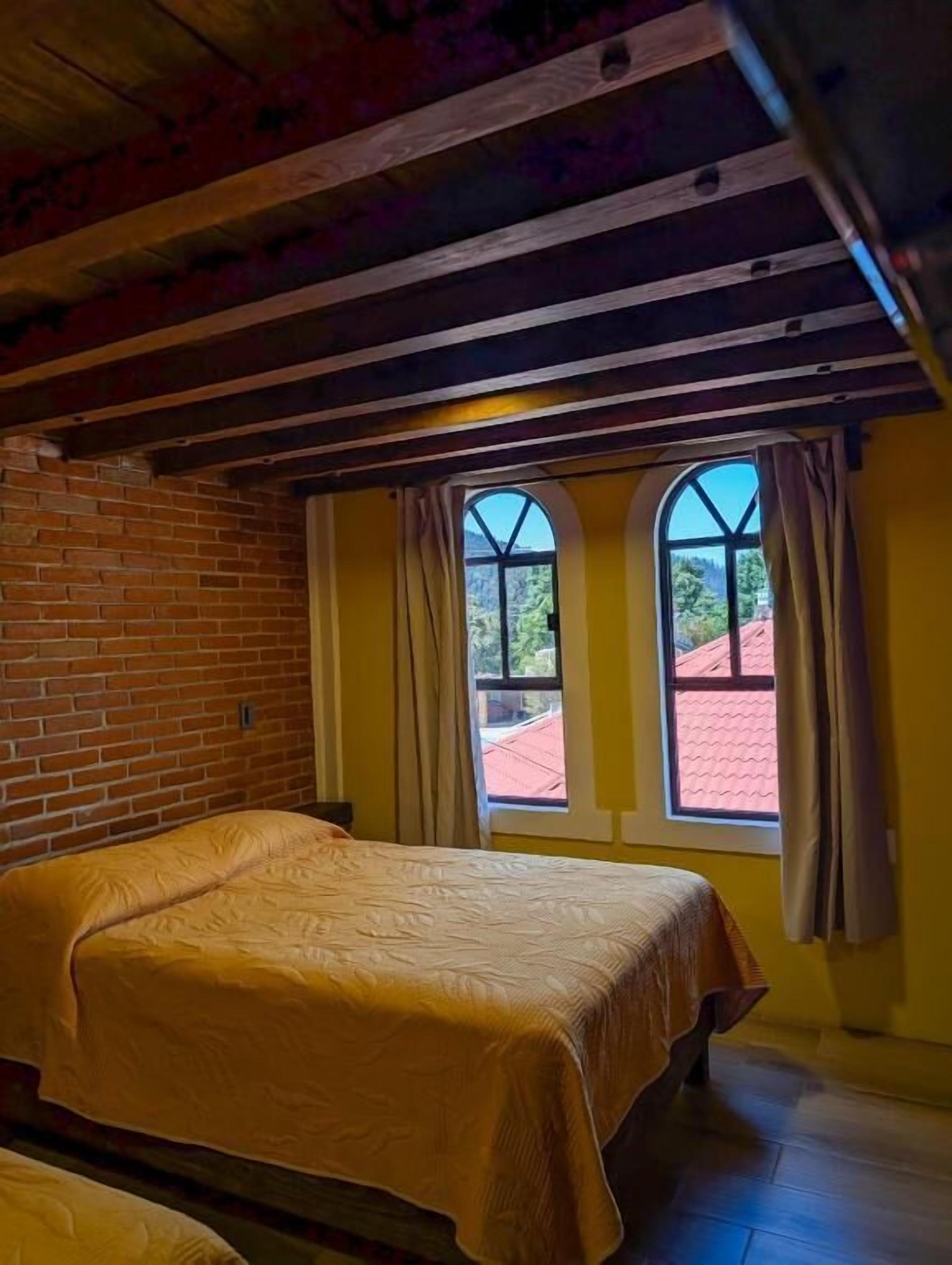 Ein Zimmer mit einem Bett, einem fensterbelaubten Fenster und einer Ziegelwand.