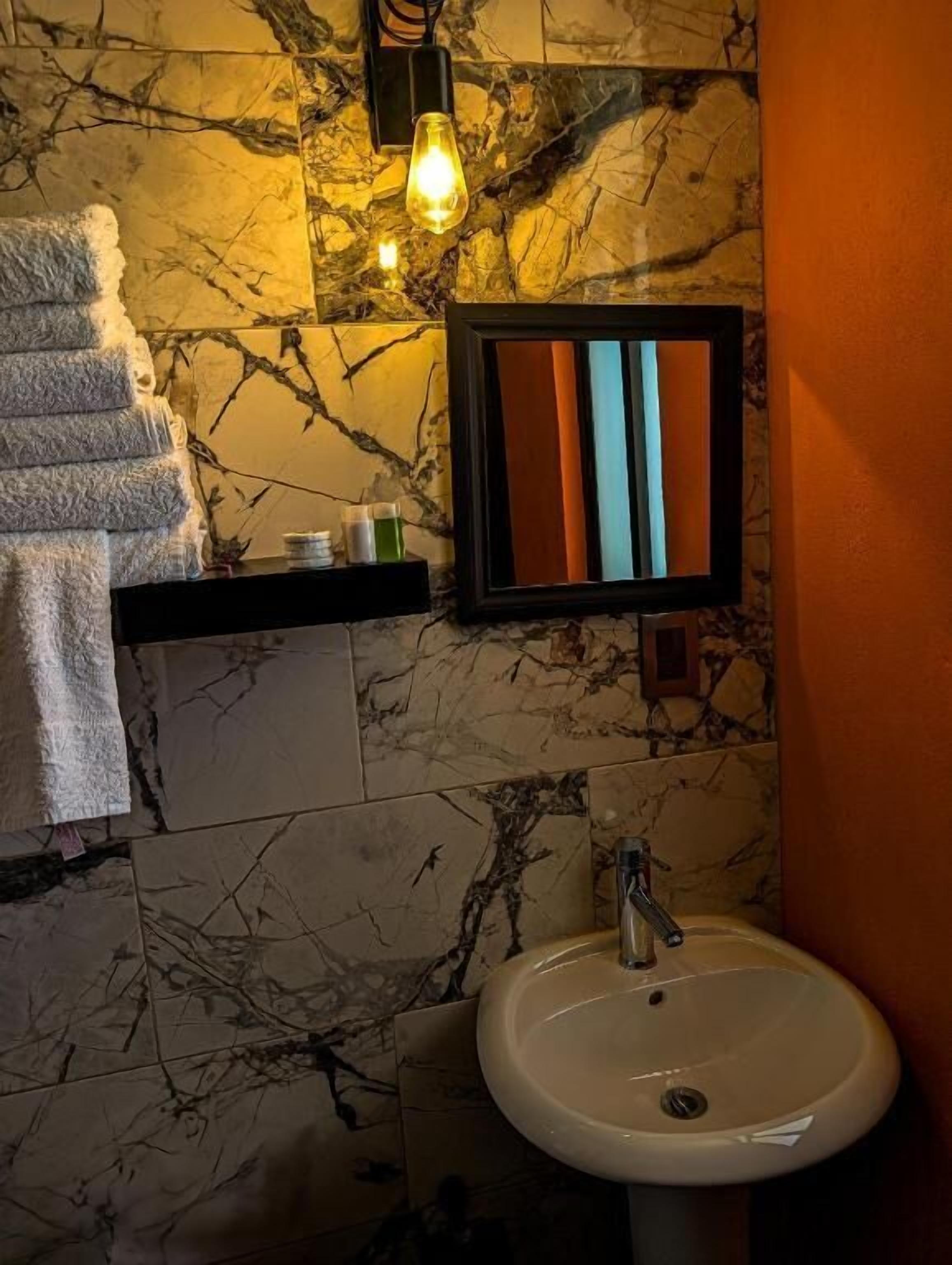 A bathroom with a marble wall, a sink, a towel rack, and a shelf with toiletries.