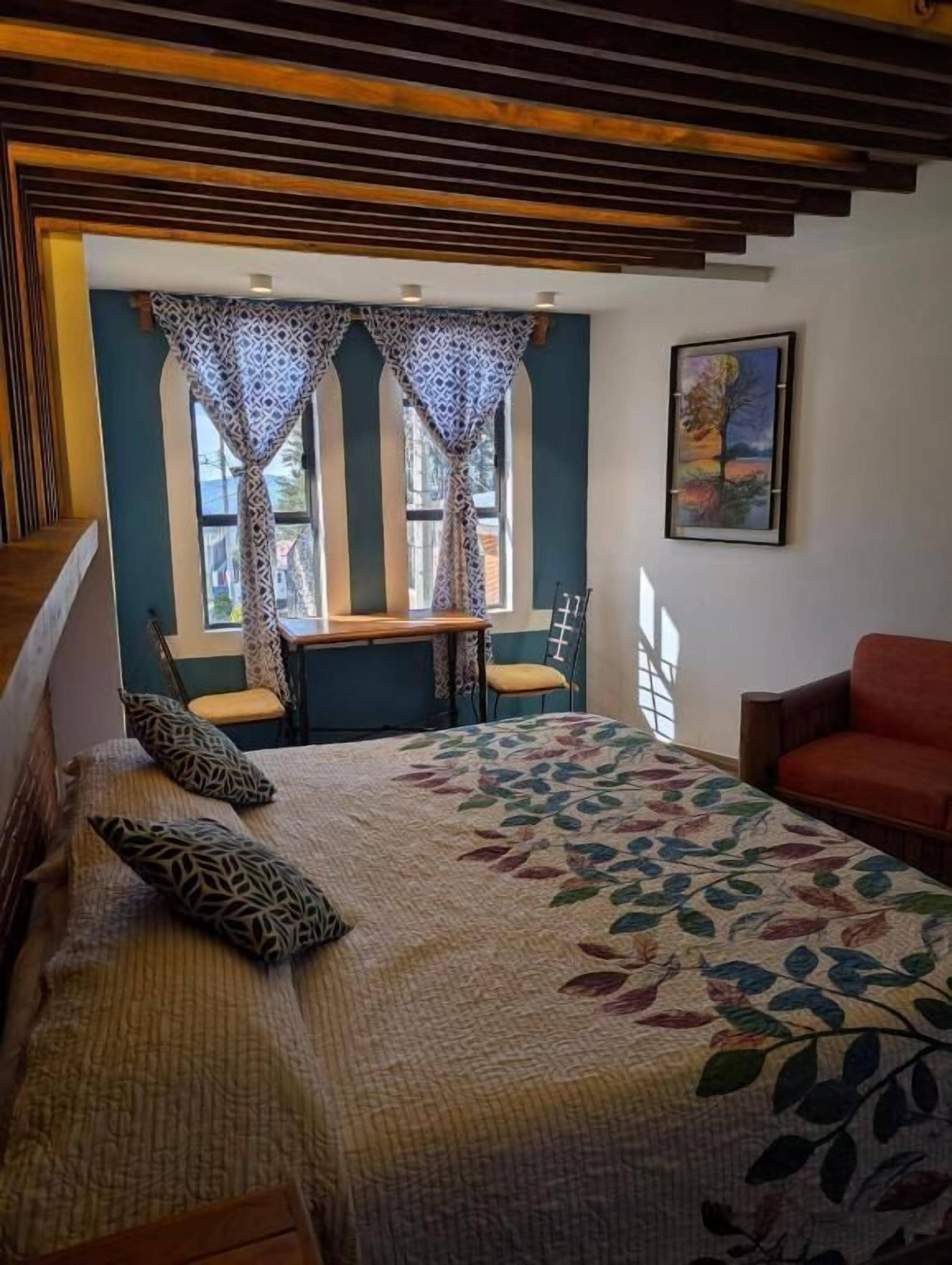 A bedroom with a bed, a desk, two chairs, and a red armchair.