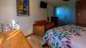 A bedroom with a wooden ceiling, a bed with a floral bedspread, a desk, and a chair.