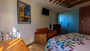 A bedroom with a wooden ceiling, a bed with a floral bedspread, a desk, and a chair.