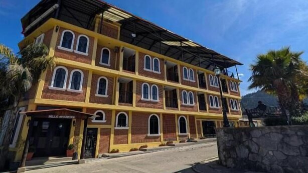 A multi-story building with a flat roof, a stone wall in front, and a clear blue sky.