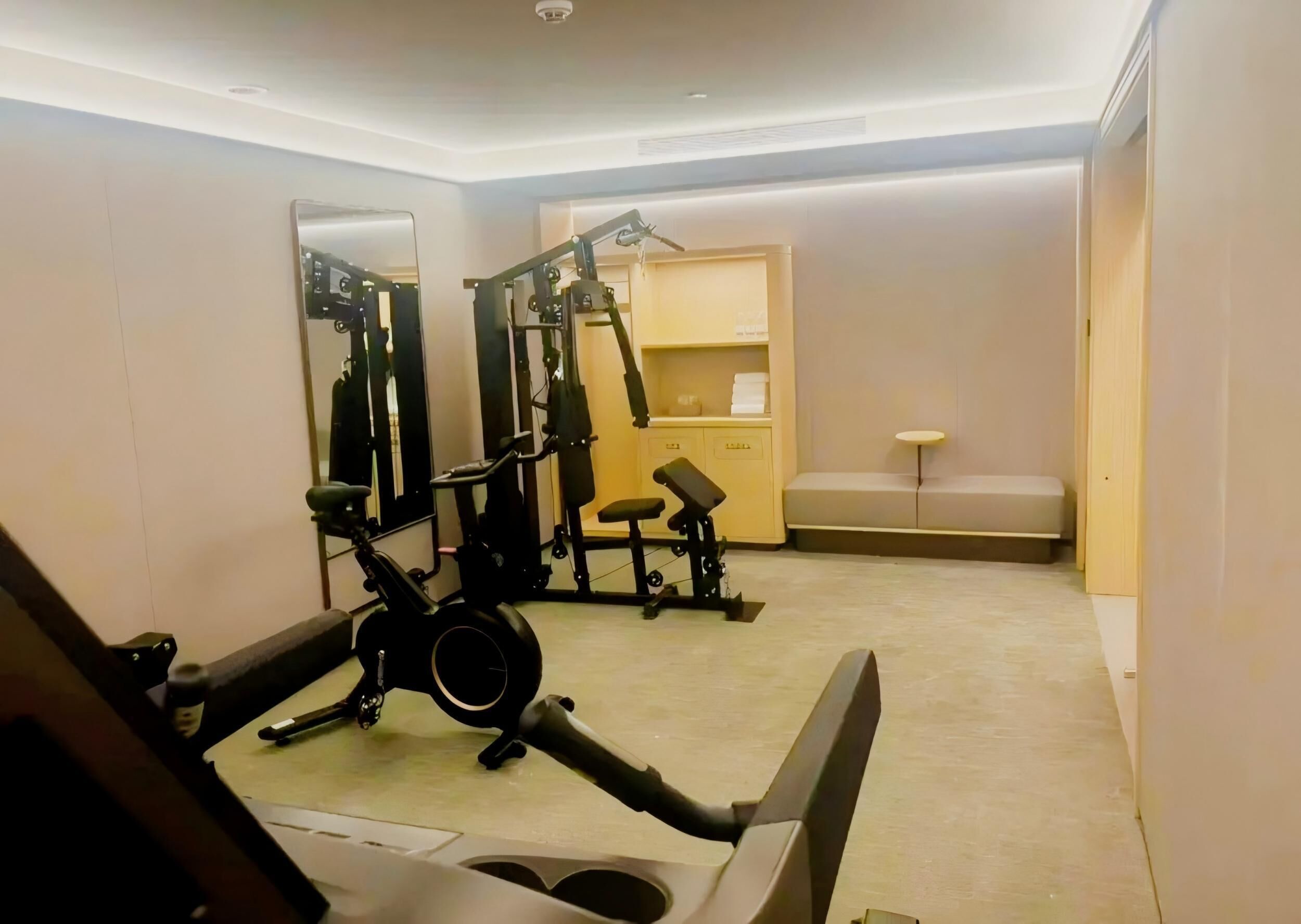 Un gimnasio con equipo de ejercicio, un espejo, una banca y una pequeña zona de estar.