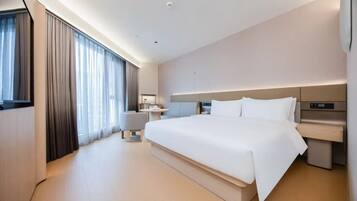 A modern hotel room with a large bed, a desk, and a seating area.