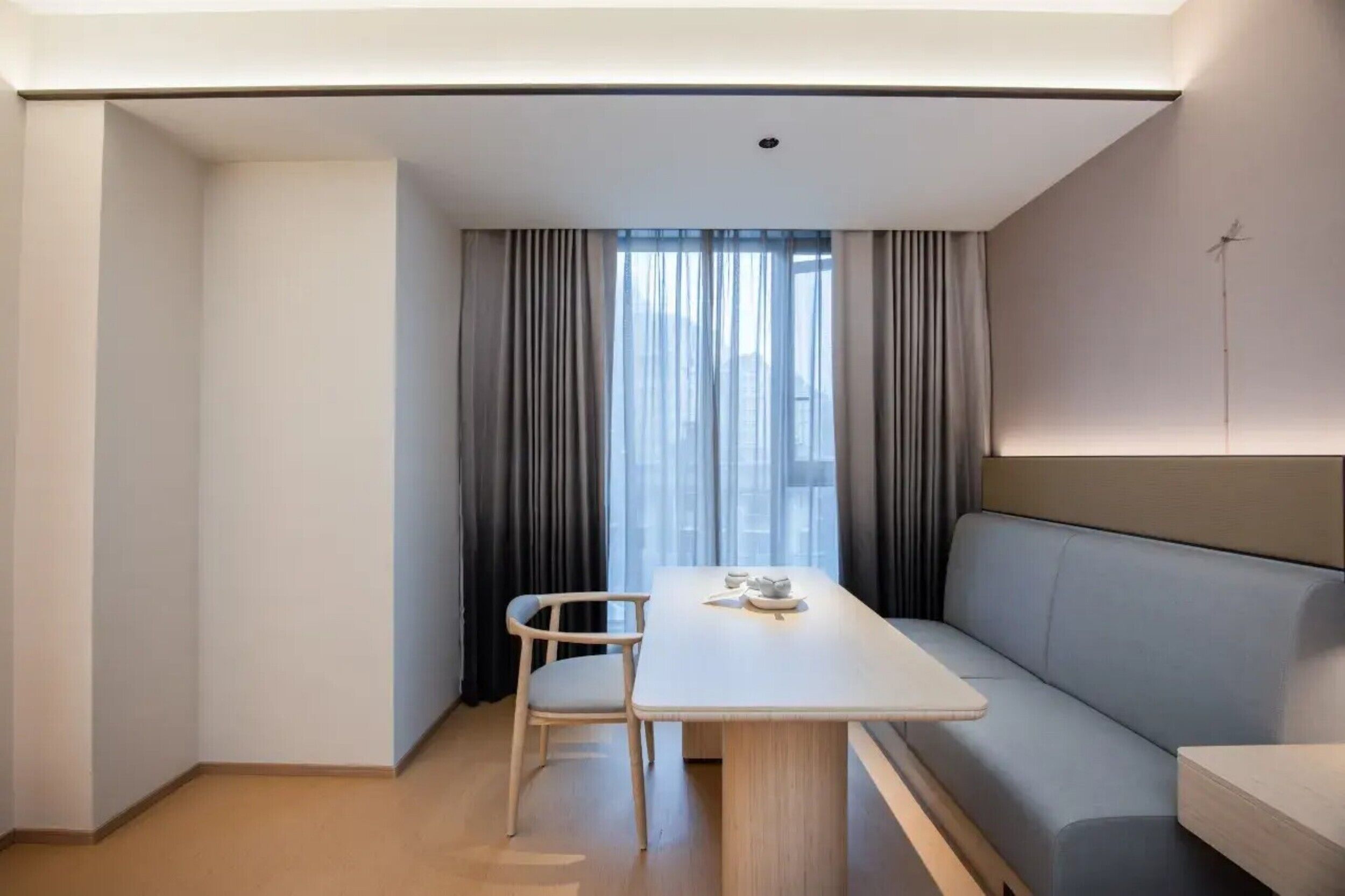 Habitació moderna i senzilla amb taula blanca, sofà gris i finestra amb cortines.