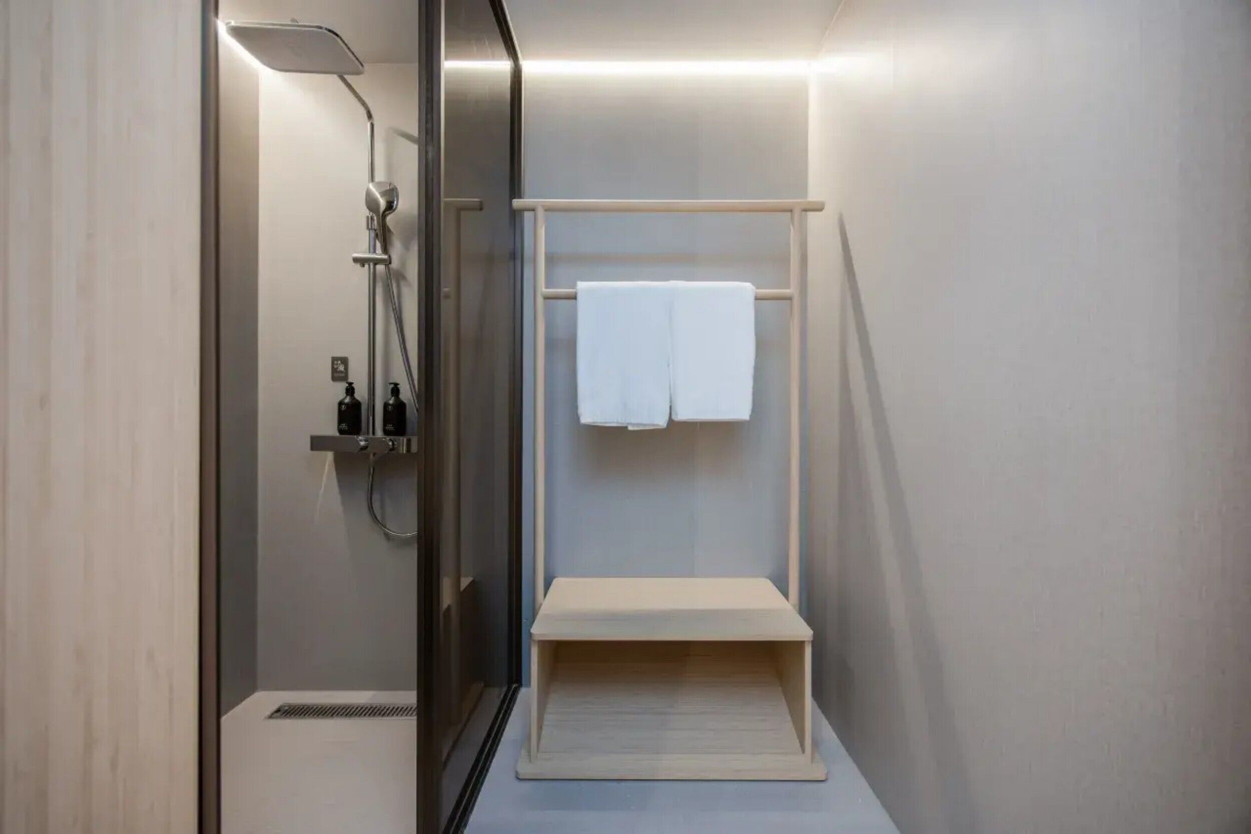 Un baño moderno con cabina de ducha de vidrio, un perchero con una toalla blanca y un estante pequeño.