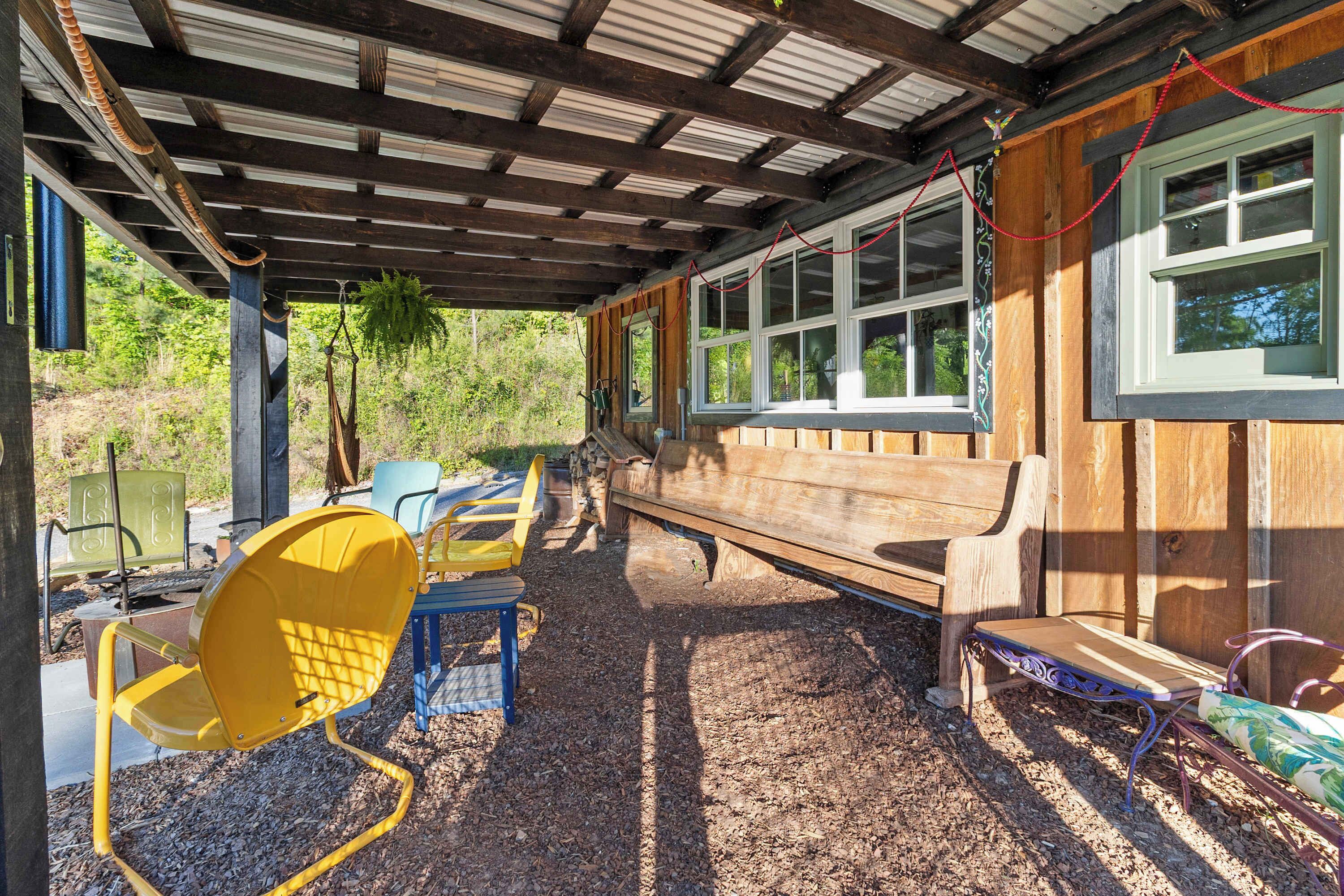 A covered outdoor seating area with a bench, chairs, and a table.