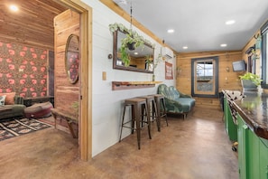 A cozy interior with a wooden ceiling, a kitchen area with stools, a green sofa, and a patterned wall. - Meadowlark: Adventure Bunkhouse Near Downtown (Chattanooga)