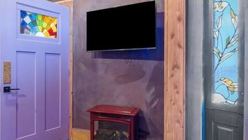 A room with a wooden ceiling, a purple door with a stained glass window, a black flat-screen TV mounted on the wall, and a small wooden table.