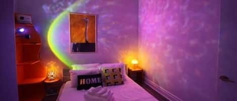 A bedroom with a bed, pillows, a wall-mounted artwork, and a nightstand with a lamp.