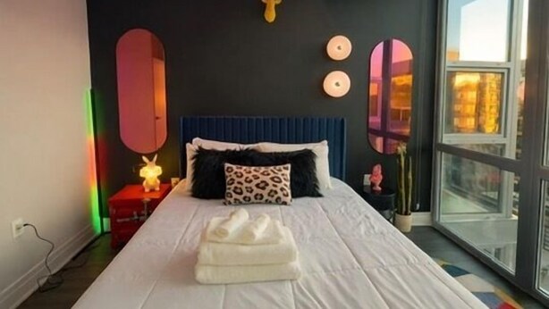 A bedroom with a bed, a headboard, a window, and a wall-mounted mirror.
