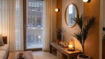 A cozy living room with a sofa, a coffee table, a lamp, a mirror, and a potted plant.