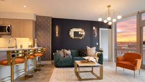 Un salon moderne avec un canapé vert, une table basse et un coin bar équipé de tabourets.