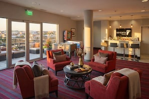 A hotel lobby with red armchairs, a foosball table, a bar area, and a city view through large windows. - Shaw 2BR | Private Projector Cinema, Rooftop & Fitness (washington)