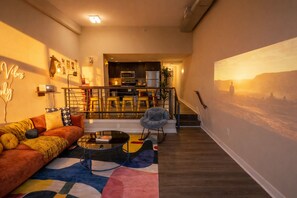 A living room with a sofa, a coffee table, and a chair. There is a staircase leading to a kitchen area. - Shaw 2BR | Private Projector Cinema, Rooftop & Fitness (washington)