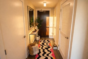 A hallway with a mirror, a console table with a vase and candles, a potted plant, a woven basket, and a zebra-striped rug. - Shaw 2BR | Private Projector Cinema, Rooftop & Fitness (washington)
