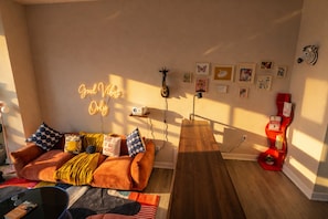 A cozy living room with a sofa, a wooden coffee table, a neon sign, and various wall art. - Shaw 2BR | Private Projector Cinema, Rooftop & Fitness (washington)