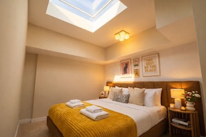A bedroom with a skylight, a bed with a yellow blanket, a headboard, bedside lamps, and framed pictures on the wall. - Shaw 2BR | Private Projector Cinema, Rooftop & Fitness (washington)