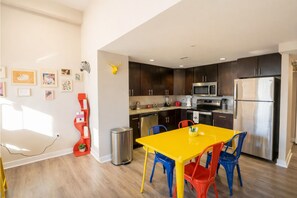 A modern kitchen with dark wood cabinets, stainless steel appliances, and a yellow table with blue and red chairs. - Shaw 2BR | Private Projector Cinema, Rooftop & Fitness (washington)