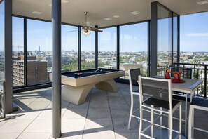A pool table and chairs on a balcony with a city view.