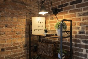 A brick wall with a shelf holding a sign, a book, and a plant.