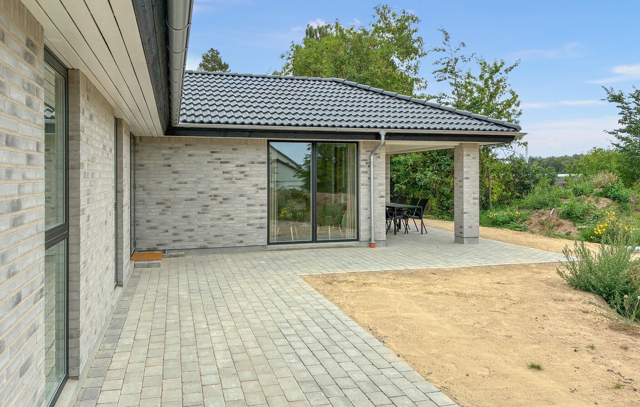 Une maison moderne avec une façade en briques, un toit en tuiles et un patio couvert comprenant une table et des chaises.
