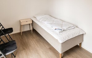 A single bed with a white mattress and a matching pillow, a small wooden nightstand, and a black chair. - Gorgeous home in Gilleleje with sauna (Gilleleje)