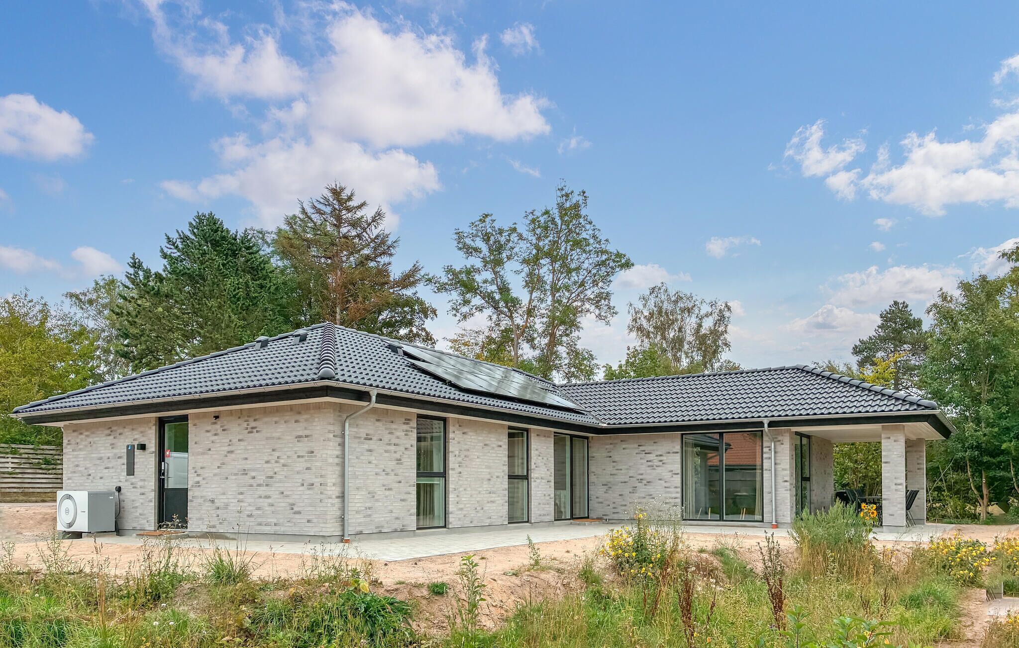 Ein modernes, zweistöckiges Haus mit Ziegelaußenwand, großen Fenstern und einer überdachten Veranda.