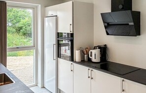 A modern kitchen with a built-in refrigerator, oven, and microwave. There is a window with a view of greenery outside. - Gorgeous home in Gilleleje with sauna (Gilleleje)