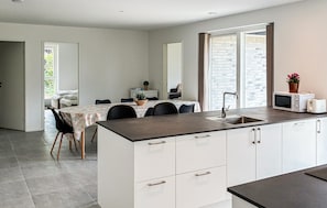 A modern kitchen with a central island, white cabinetry, and a dining area with a table and chairs. - Gorgeous home in Gilleleje with sauna (Gilleleje)