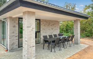 A covered outdoor dining area with a brick column, a table with chairs, and a view of greenery. - Gorgeous home in Gilleleje with sauna (Gilleleje)