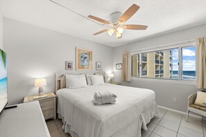 Ein Hotelzimmer mit Bett, Deckenventilator, Fenster mit Vorhängen und einem Bild an der Wand.