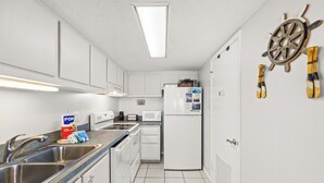A compact kitchen with white cabinets, a stainless steel sink, a microwave, and a refrigerator. - End of Summer Gulf Views at B2-407 (Panama City Beach)