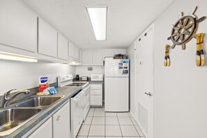 Eine kleine Küche mit weißen Schränken, einer Edelstahl-Spüle, einer Mikrowelle und einem Kühlschrank.