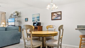 A dining area with a round wooden table, four chairs, a chandelier, and a blue sofa in the background. - End of Summer Gulf Views at B2-407 (Panama City Beach)
