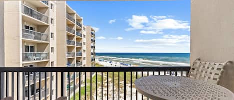 A balcony with a view of the beach and ocean, a round table, and a chair.