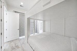 A bedroom with a bed, a door, and a window with blinds.