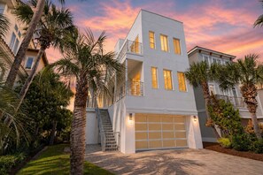 A modern two-story house with a garage, surrounded by palm trees and a sunset sky. - White Sands: Private Beach Access, HEATED Pool, Ocean Views, FREE Golf Cart (DESTIN)