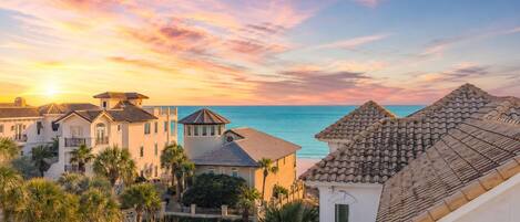 A coastal town with buildings, palm trees, and a view of the sea during sunset.