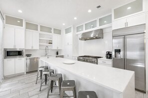A modern kitchen with white cabinetry, stainless steel appliances, and a central island with stools. - White Sands: Private Beach Access, HEATED Pool, Ocean Views, FREE Golf Cart (DESTIN)